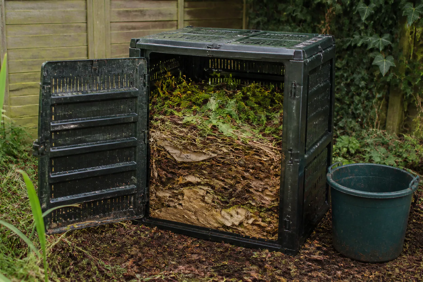 Ventilated garden compost bin containing mixed dry cardboard, stems and fresh green trimmings