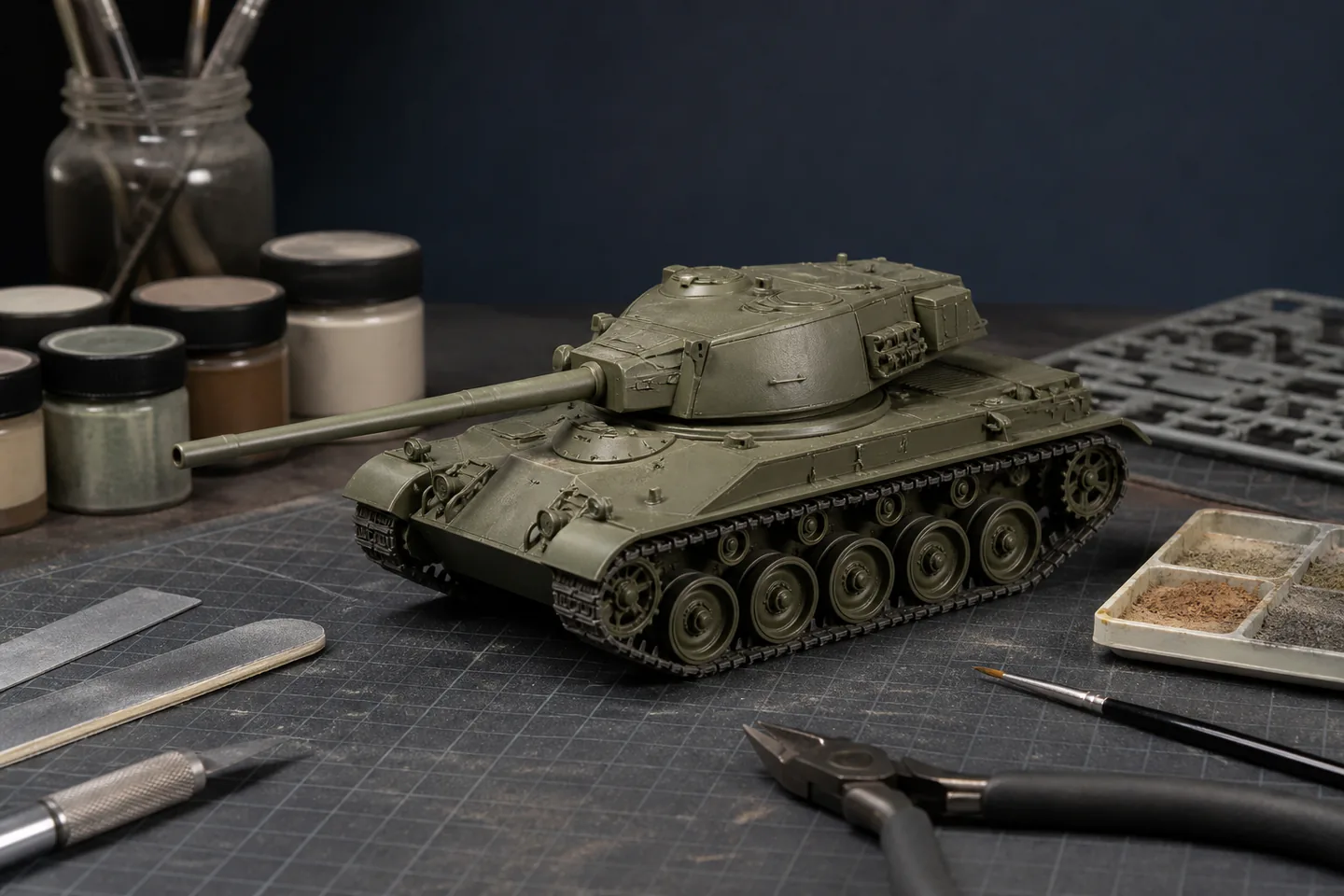 Unbranded olive scale tank model under assembly with separate tracks, sprues, cutters, brush, cement and paint on a protected bench