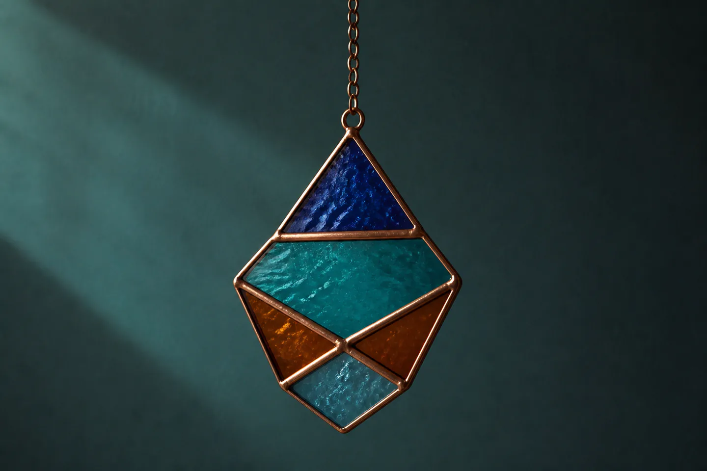 Small finished geometric copper-foil stained-glass sun catcher on a studio bench beside closed glass cutter and soldering iron in safe stand with no people, logos or text