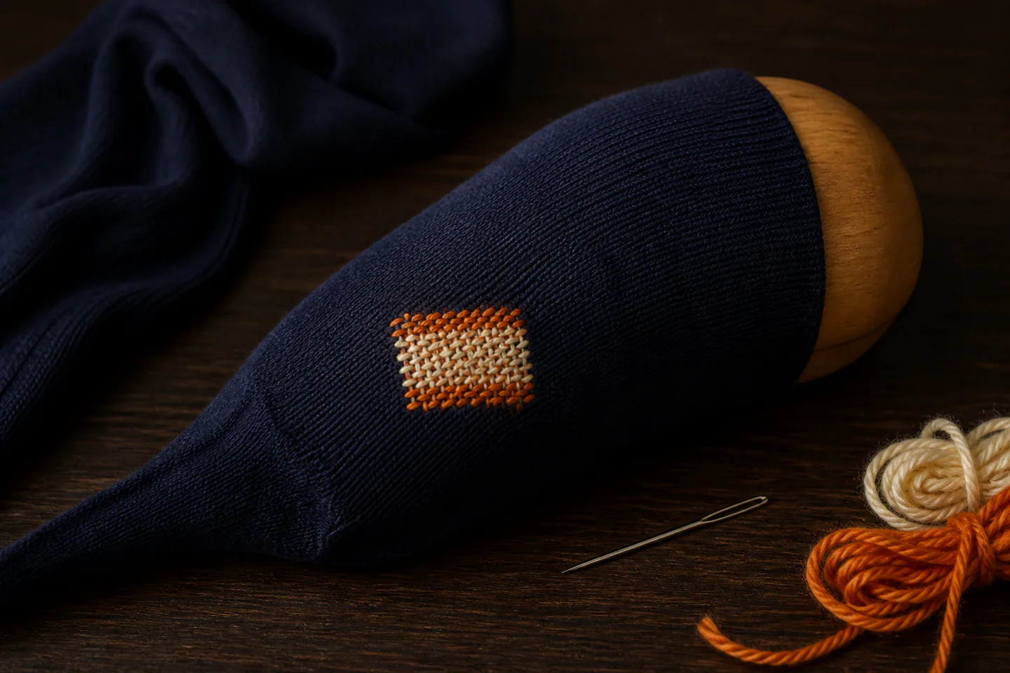 A small colourful woven darn repairing a cotton sock over a wooden darning mushroom with needle and yarn nearby